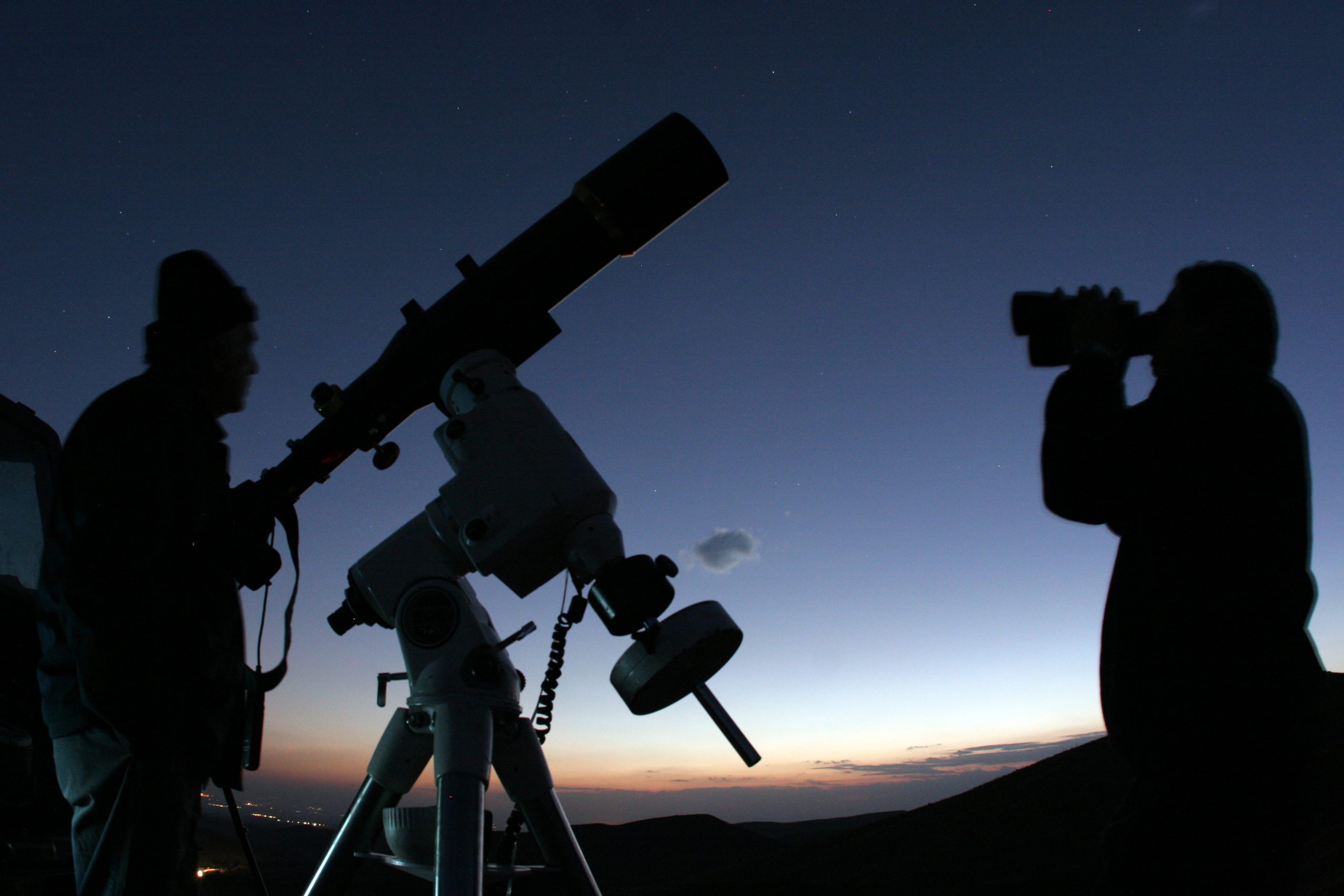 Two people in the night time, one has a telescope and the other has binoculars