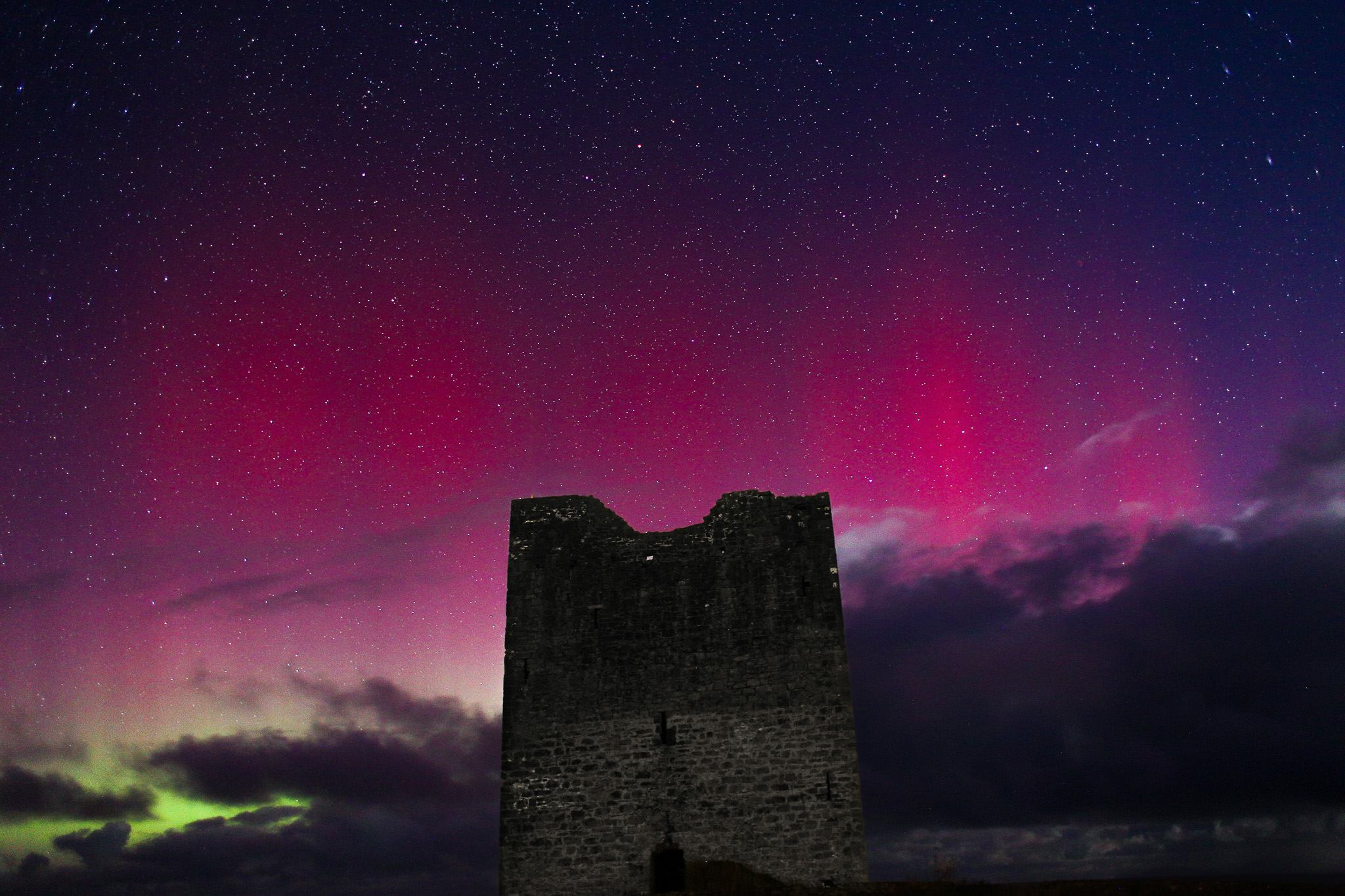 Pink and green aurora behind castle ruin